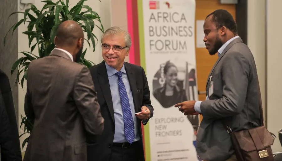 Two men talking with a colleague in front of an Africa Business Forum event banner