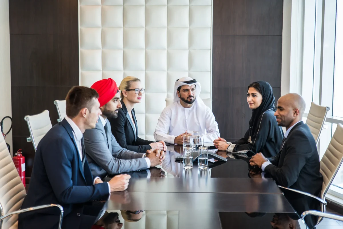 Six colleagues in business attire discussing around a conference table in an office